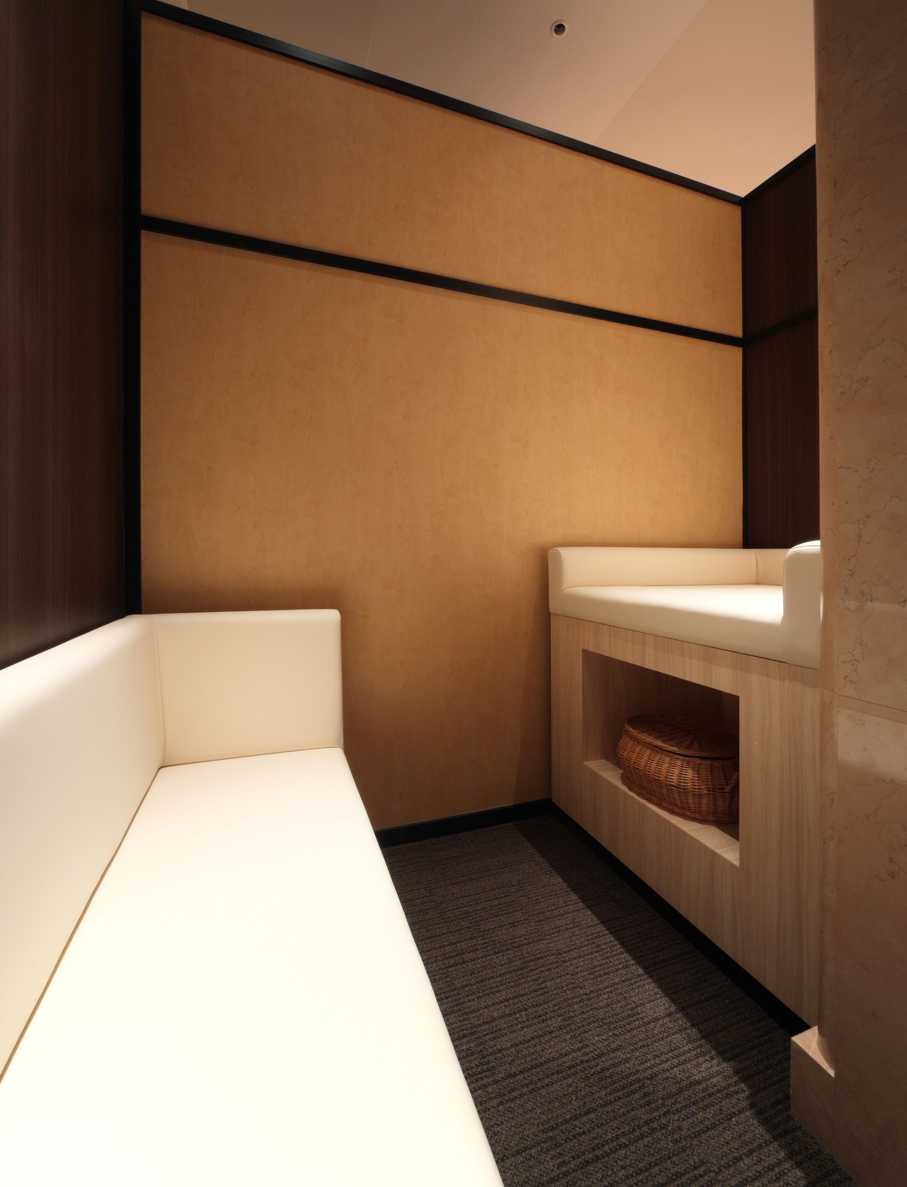 Een kleine, moderne badkamer met een witte bankje, een houten wastafelmeubel en een rieten mandje op een plank.