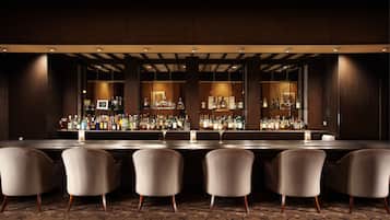 A bar area with a long counter, multiple bottles, and four chairs.