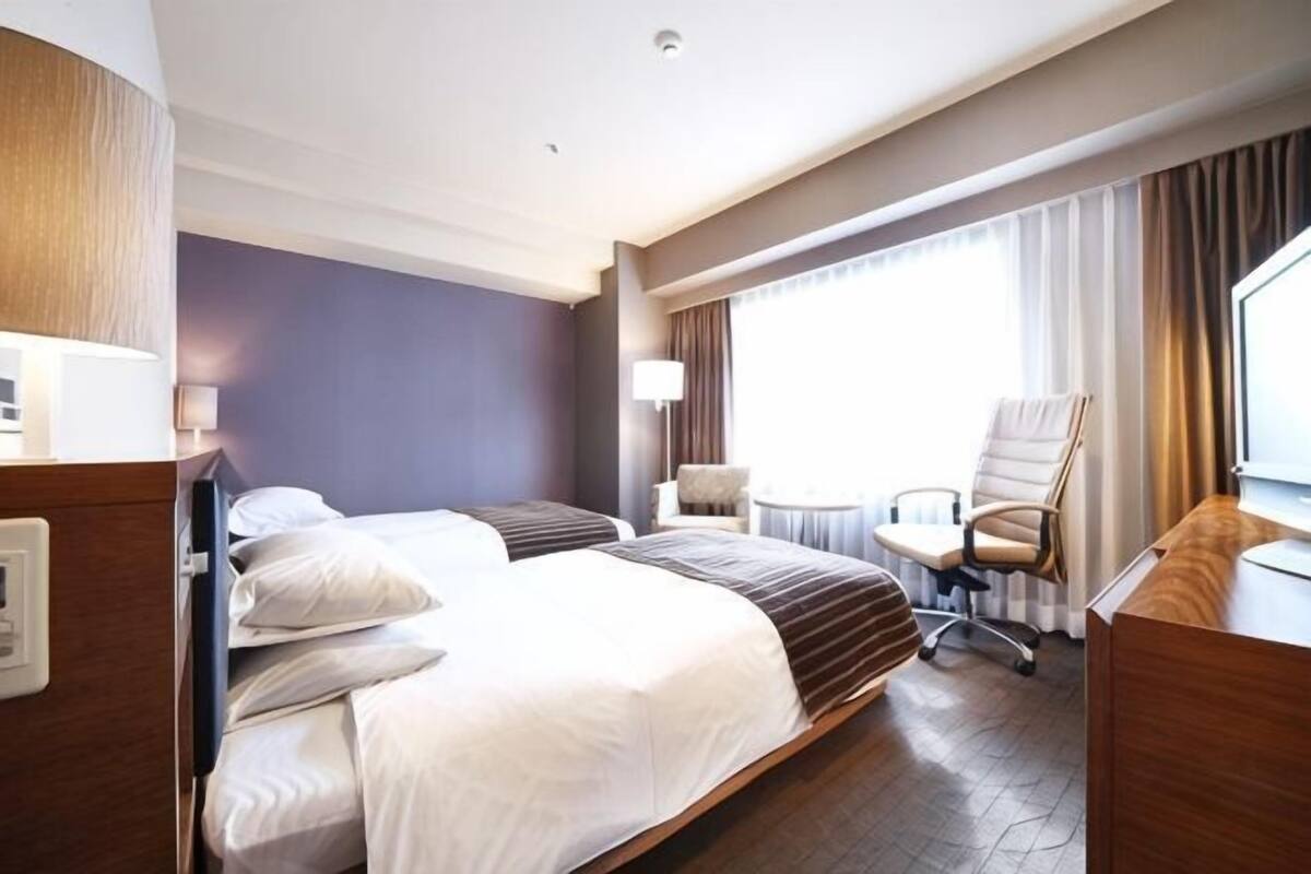 A hotel room with a large bed, a desk, a chair, and a window with curtains.