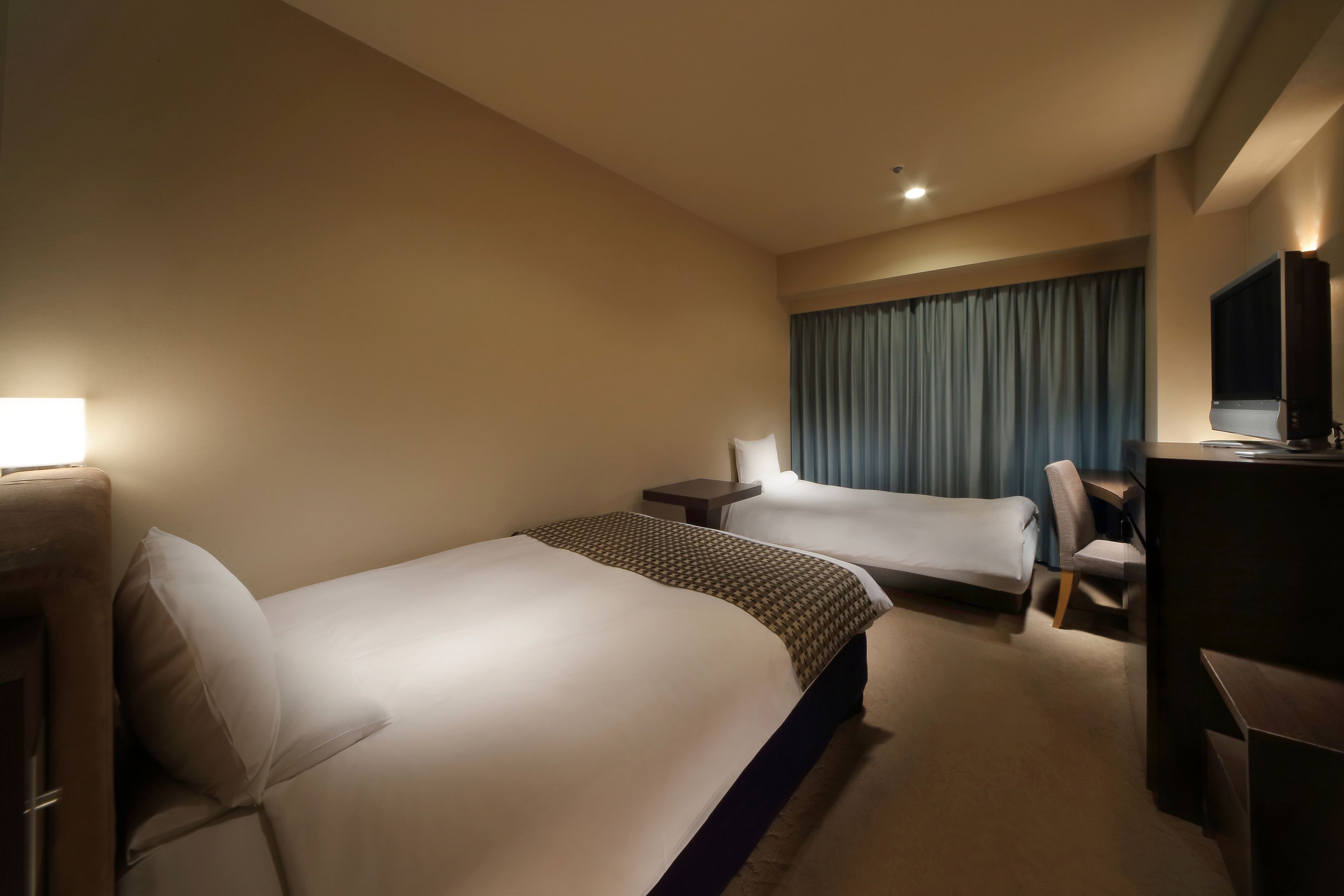 A hotel room with two beds, a desk, a chair, and a TV.