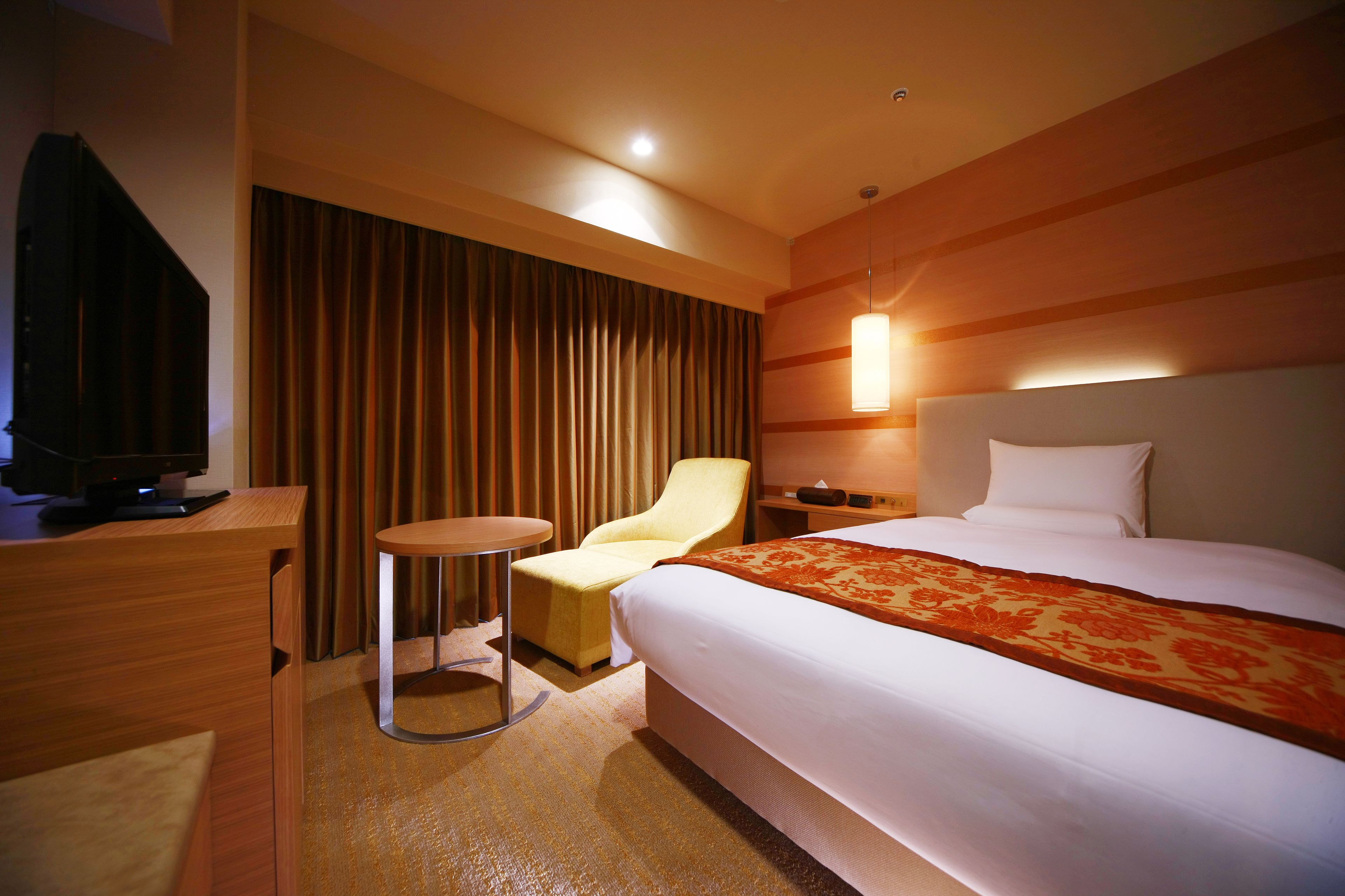 A hotel room with a bed, a desk, a chair, and a television.
