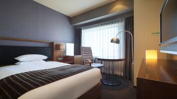 Hotellihuone, jossa on suuri sänky, työpöytä, tuoli, lamppu ja televisio.