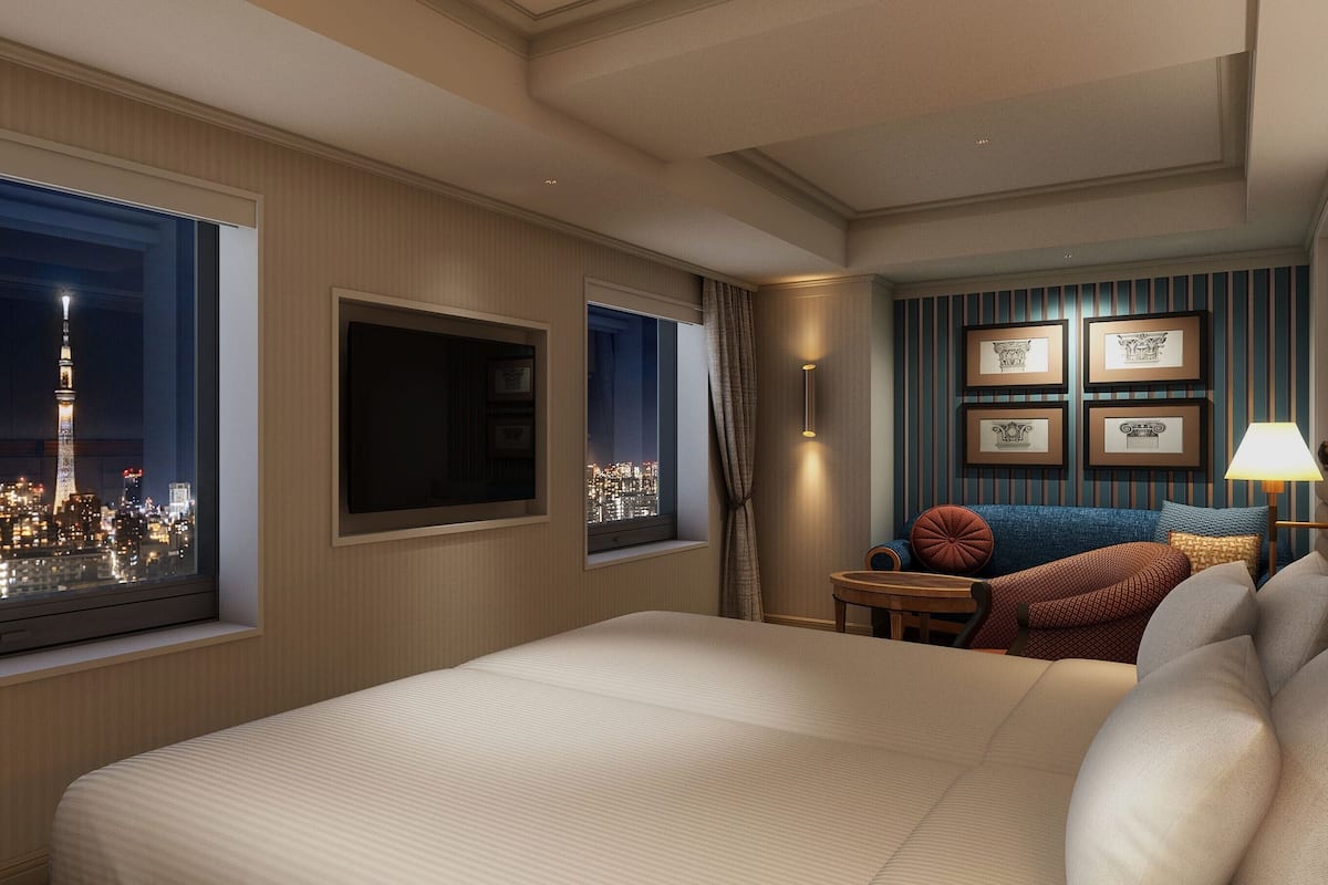 A hotel room with a large bed, a TV, a city view, a small table, and a sofa.