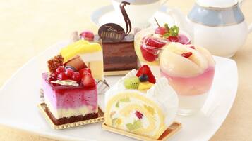 Una variedad de postres en una bandeja, incluyendo un pastel en capas, un bizcocho enrollado y un parfait, con una tetera y una taza al fondo.