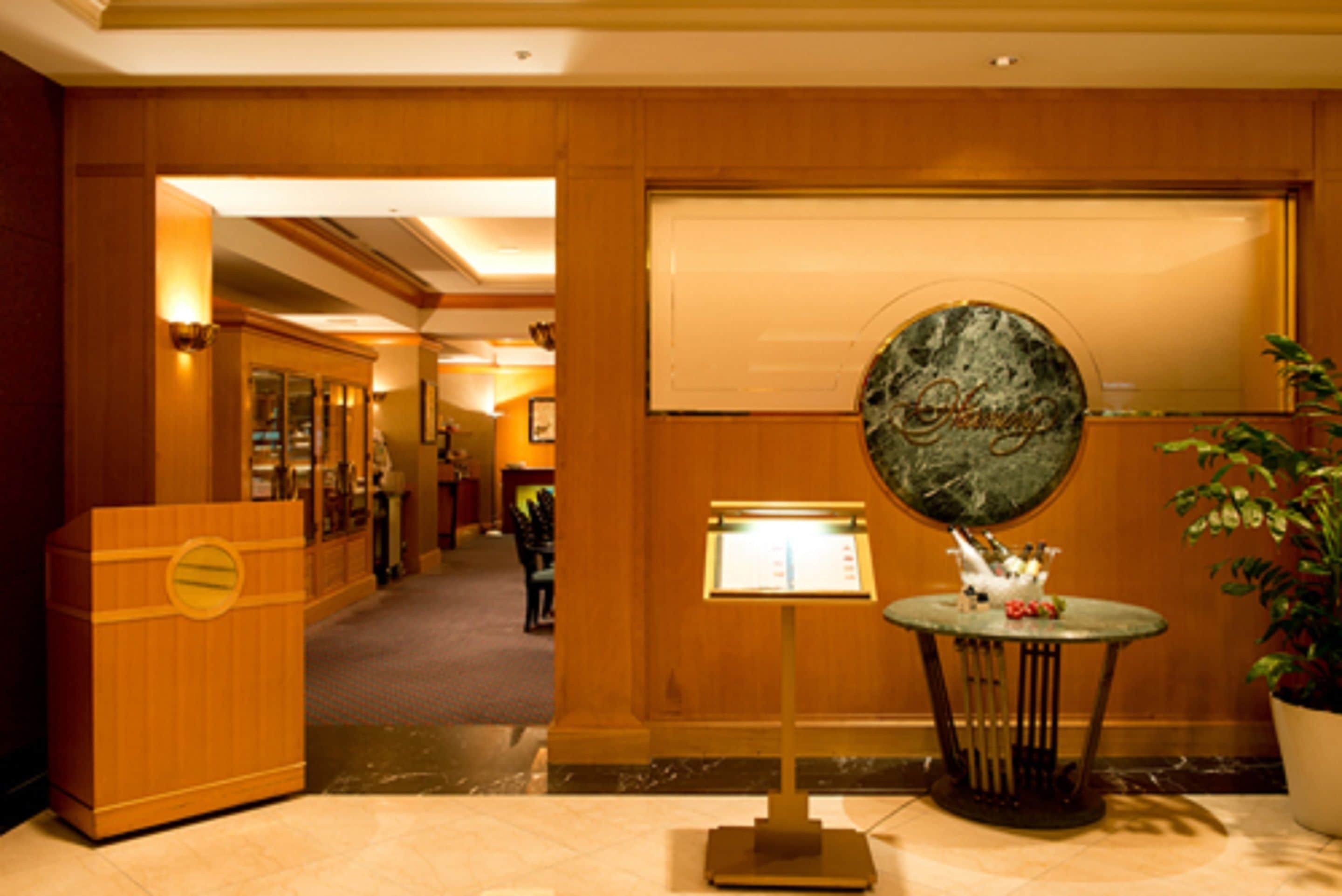 A hotel lobby with a reception desk, a digital information kiosk, a decorative stone wall, and a potted plant.