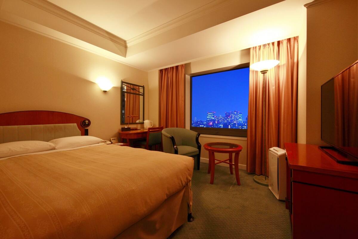 A hotel room with a large bed, a desk with a chair, a television, and a window with curtains.