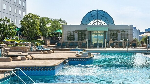 A hotel pool area with a large water fountain, lounge chairs, and a modern building with a dome structure in the background. - Hotel East 21 Tokyo (Tokyo)