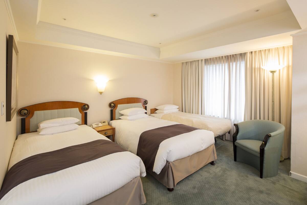 A hotel room with three beds, a chair, and a lamp.