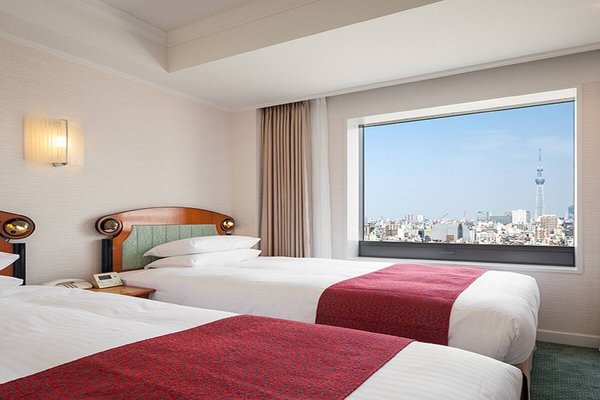 A hotel room with two beds, a city view, and a large window.