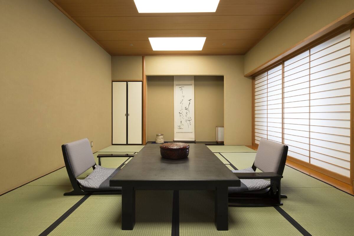 A traditional Japanese meeting room with tatami flooring, a low table, two chairs, sliding doors, and a shoji screen.