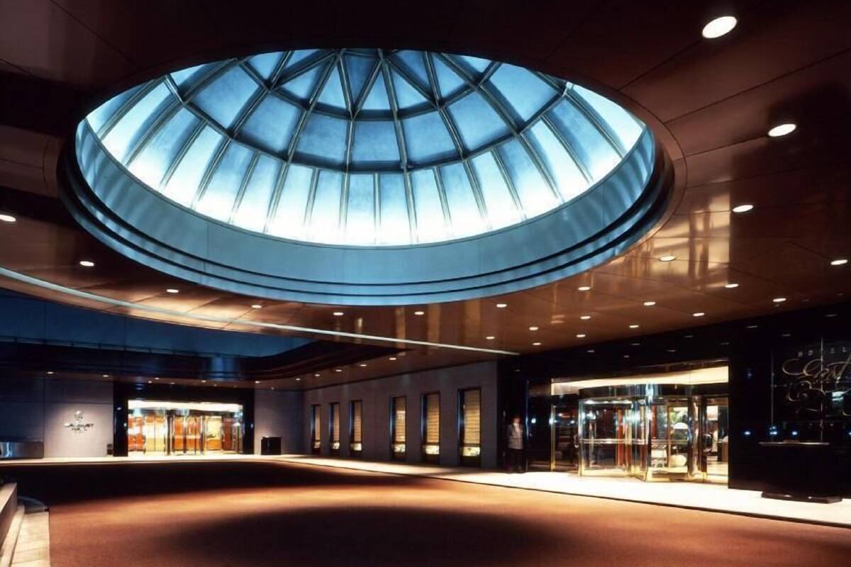 A modern hotel lobby with a large skylight, a reception area, and a glass entrance.