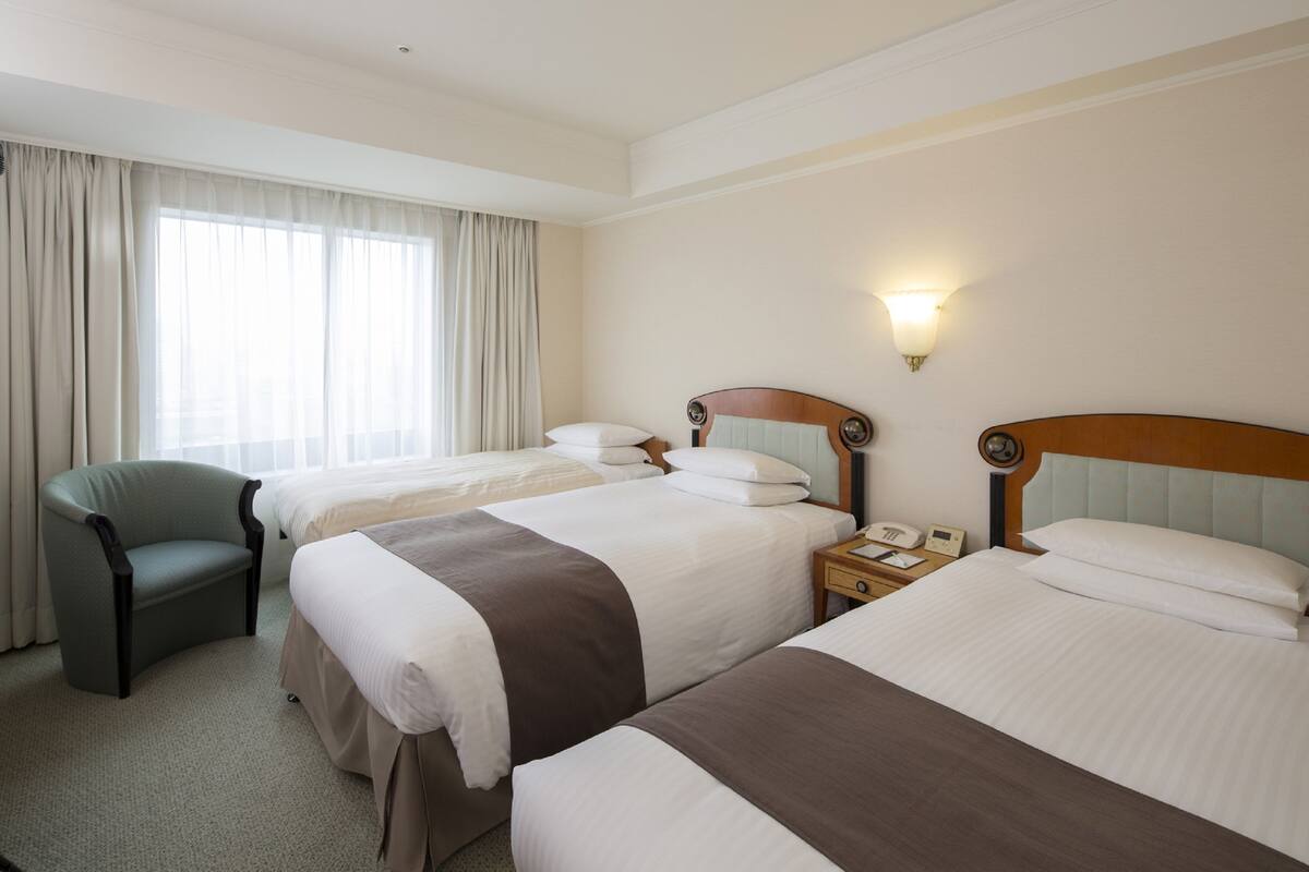 A hotel room with two beds, a chair, a bedside table with a phone, and a window with curtains.