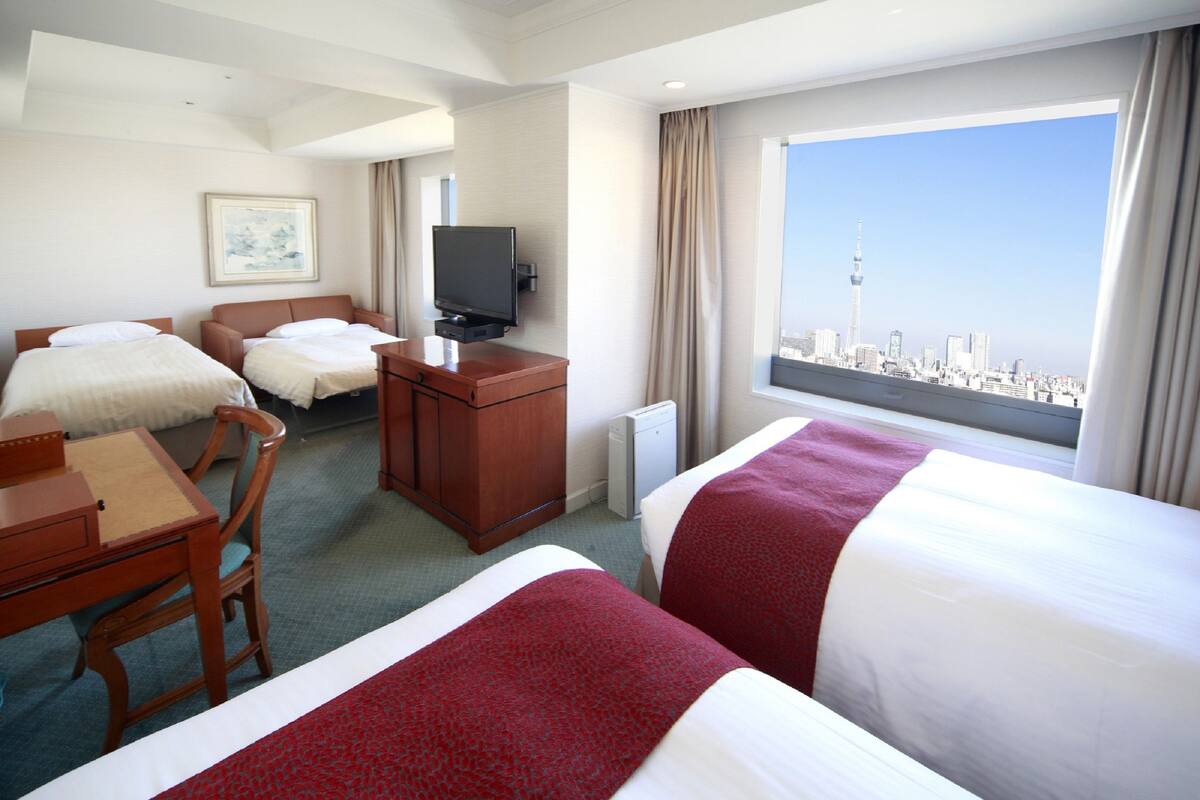 A hotel room with two beds, a desk, a television, and a city view.