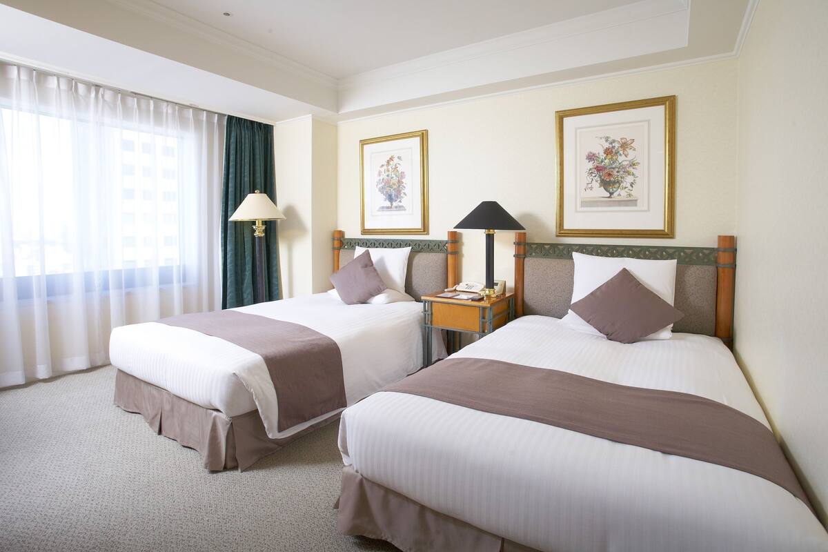 A hotel room with two beds, a nightstand, a lamp, and framed artwork on the wall.
