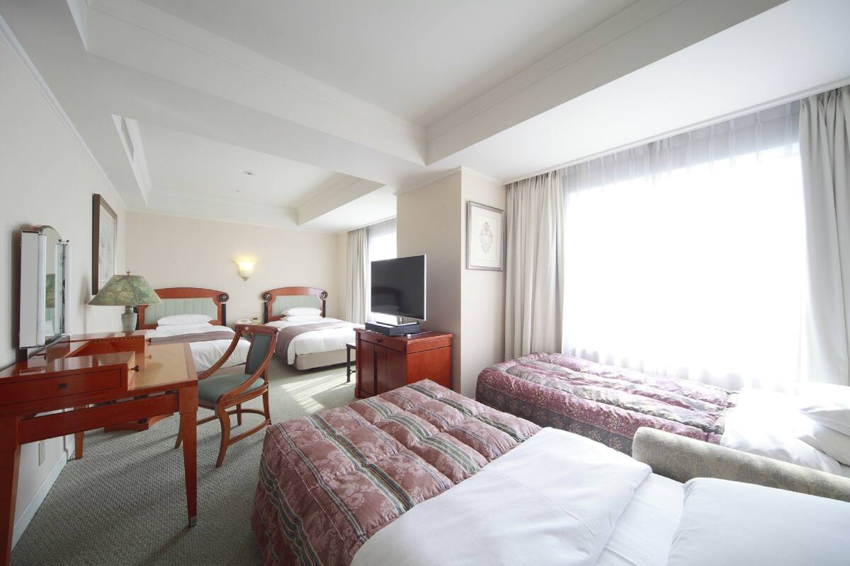 A hotel room with two beds, a desk, a chair, a television, and a window with curtains.