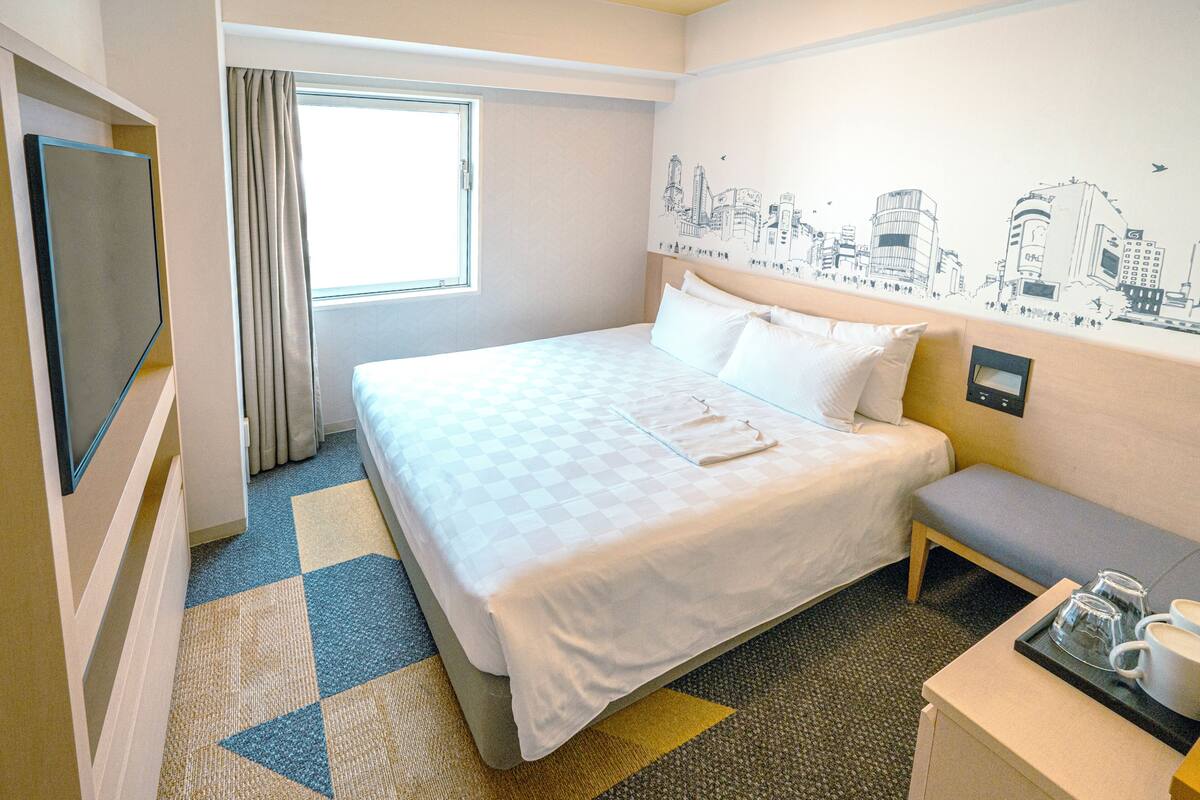 Ein Hotelzimmer mit einem Bett, einer Bank, einem Fernseher und einem Fenster mit Vorhängen.