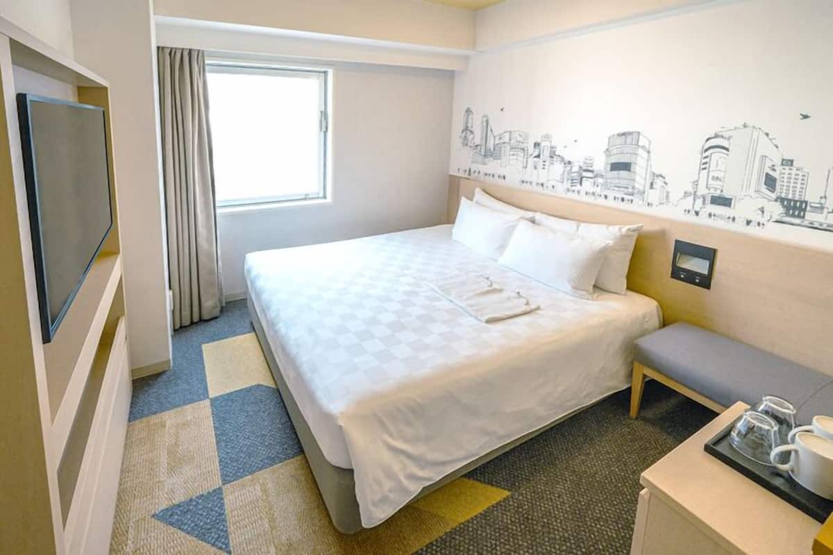 A hotel room with a bed, a bench, a TV, a window with curtains, and a cityscape wall mural.