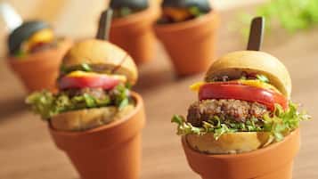 A series of terracotta cups containing burgers with lettuce, tomato, and a yellow sauce, arranged on a wooden surface.