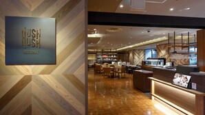 Een modern restaurantinterieur met een houten visgraatvloer, een receptiebalie en een eetgedeelte met tafels en stoelen.