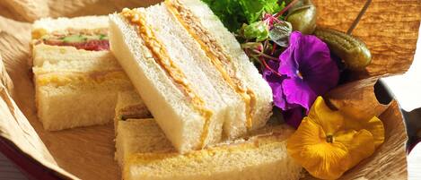 A wooden tray with sandwiches, a pickle, and some flowers.