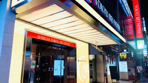 Het uiterlijk van het Shibuya Tokyo Rei Hotel, met verlichte reclameborden en een rode loper entree.