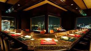 A long dining table with multiple chairs, set with wine glasses and menus, in a room with large windows offering a city view. - Ginza Creston (Tokyo)