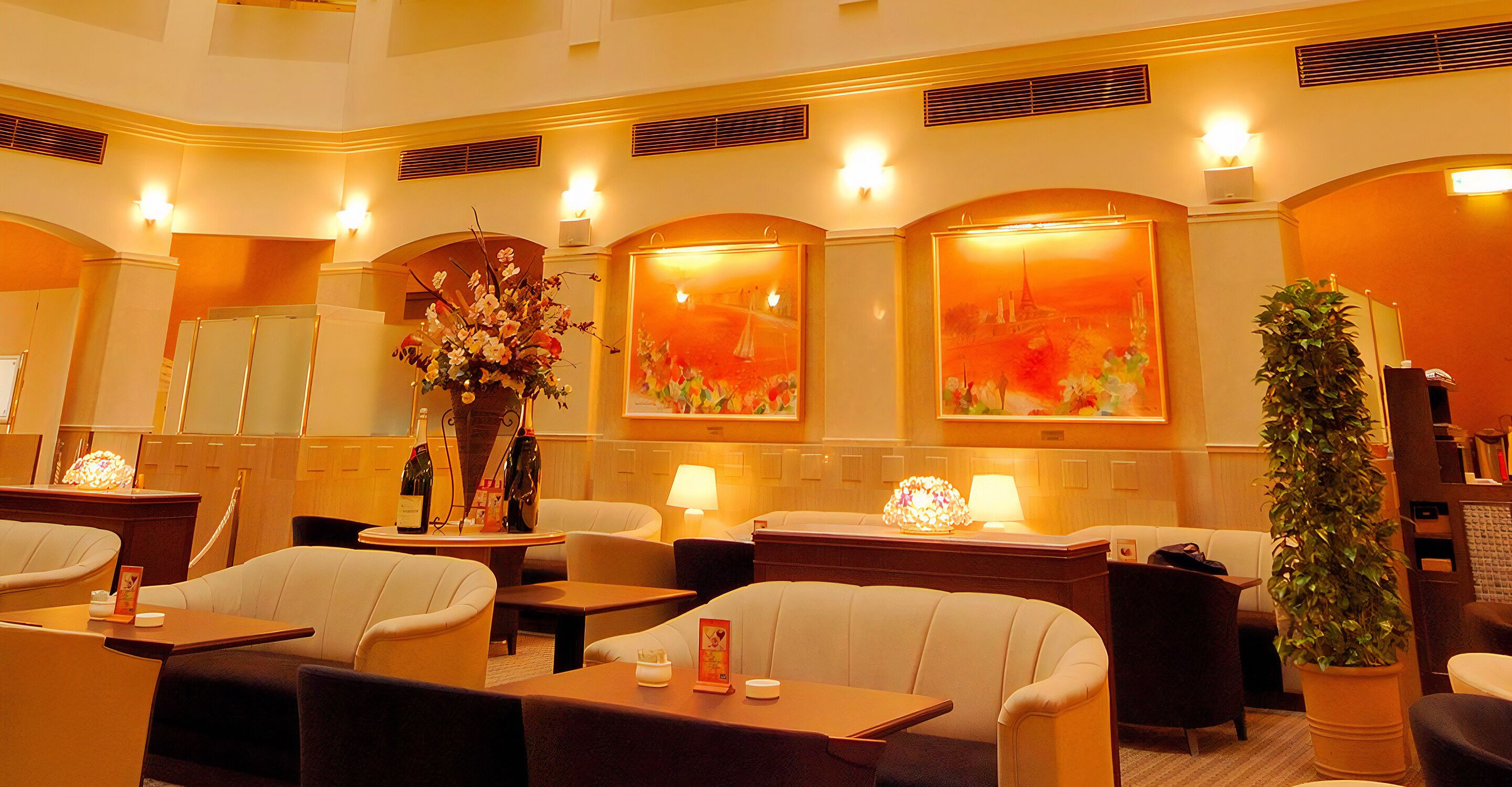 Un vestíbulo de hotel con zonas de estar, un mostrador de recepción y elementos decorativos como flores y obras de arte.