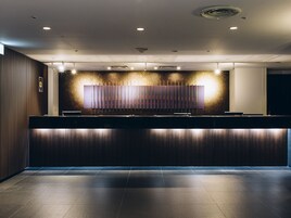 Un moderno mostrador de recepción con acabado en madera oscura, iluminación empotrada y una gran pantalla mural.
