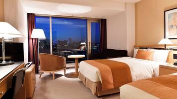 A hotel room with a large bed, a desk with a TV, a chair, a small table, and a view of the city at night.