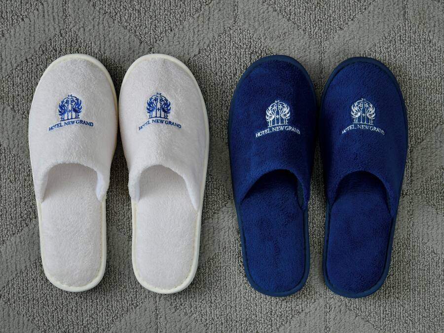 Une paire de pantoufles blanches et bleues ornées d’un logo, posées sur une surface texturée.