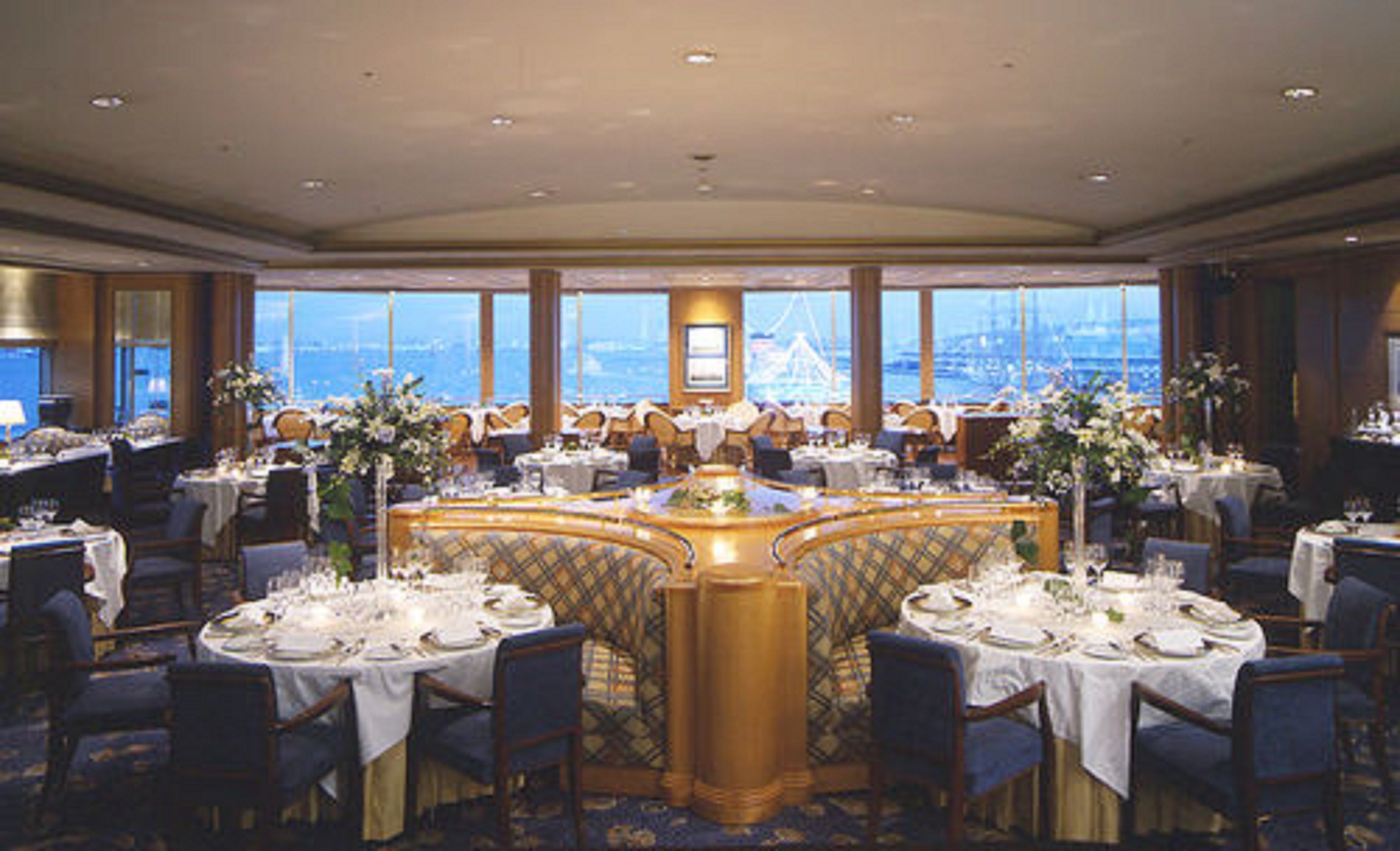 A formal dining room with round tables, chairs, and a view of a bridge and water.