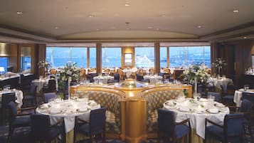 A formal dining room with round tables, chairs, and a view of a bridge and water.