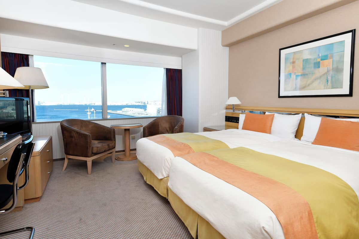 Quarto de hotel com uma cama grande, escrivaninha, cadeira e televisão.