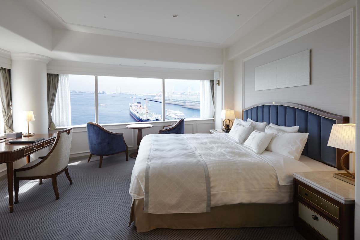 Quarto de hotel com uma cama grande, uma escrivaninha, uma cadeira e vista para o mar.