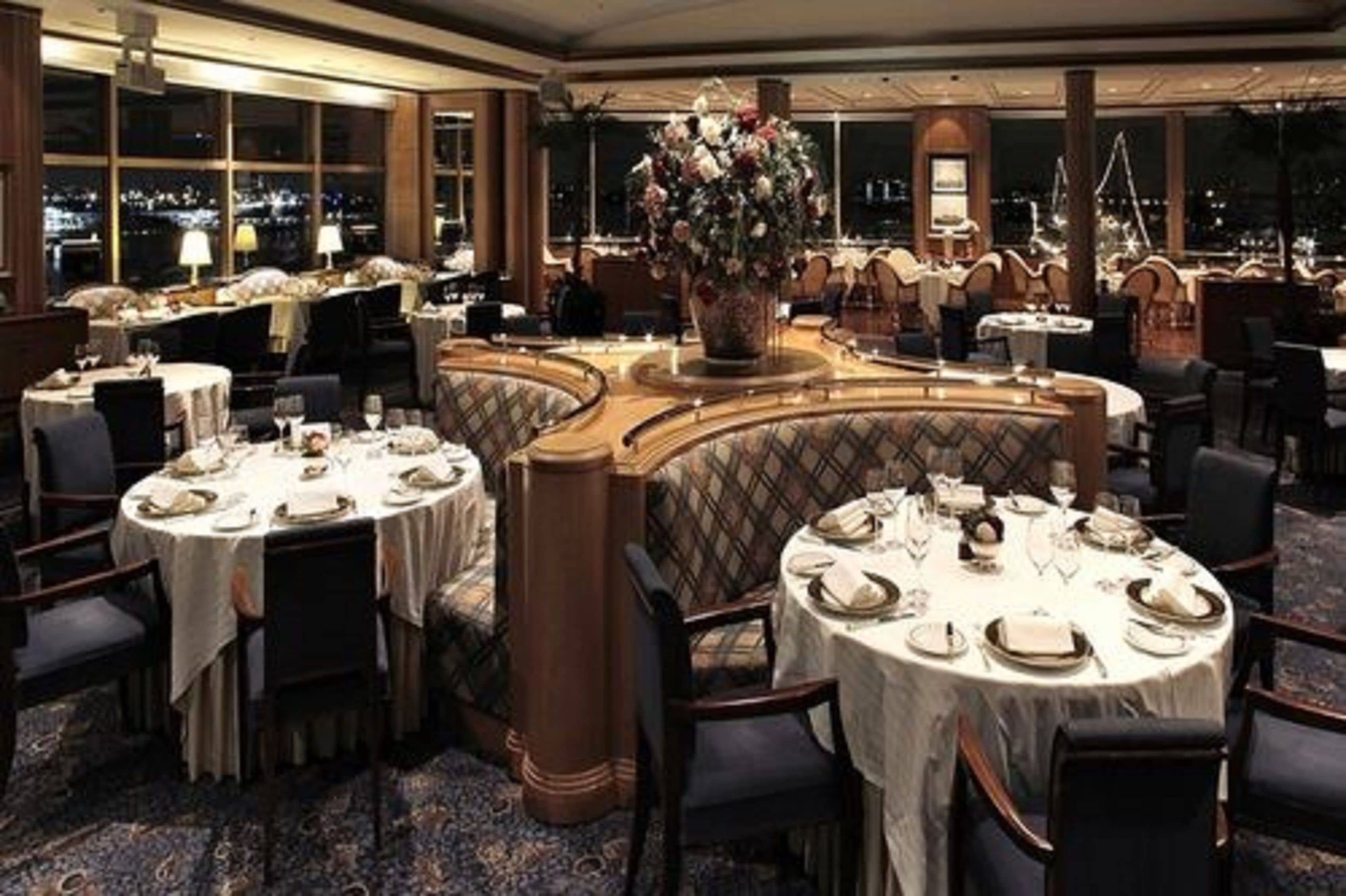 A formal dining area with round tables, chairs, and a large floral centerpiece.