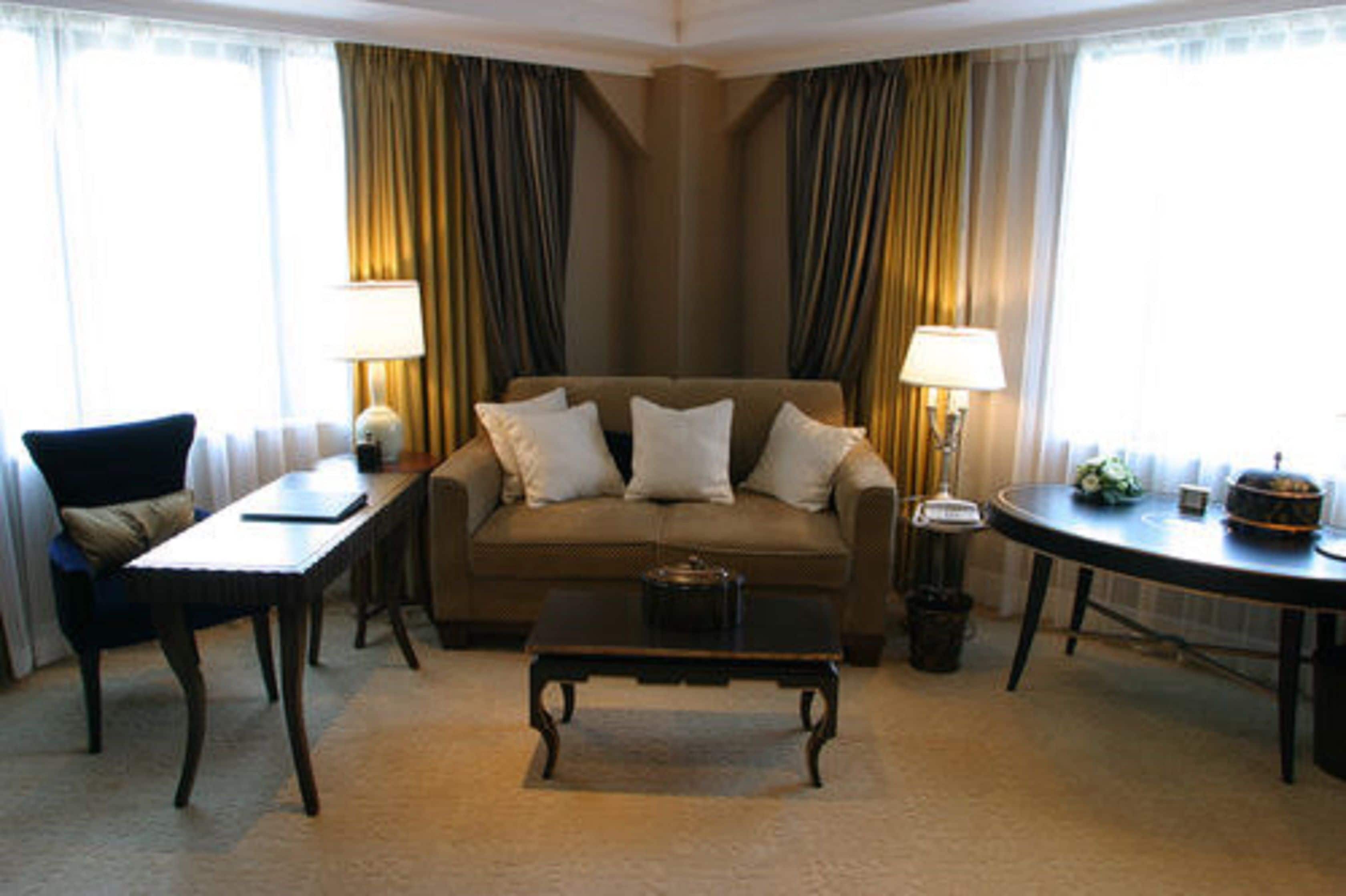 Habitación de hotel con sofá, una mesita de centro, una silla, lámpara y una pequeña mesa con un objeto decorativo.