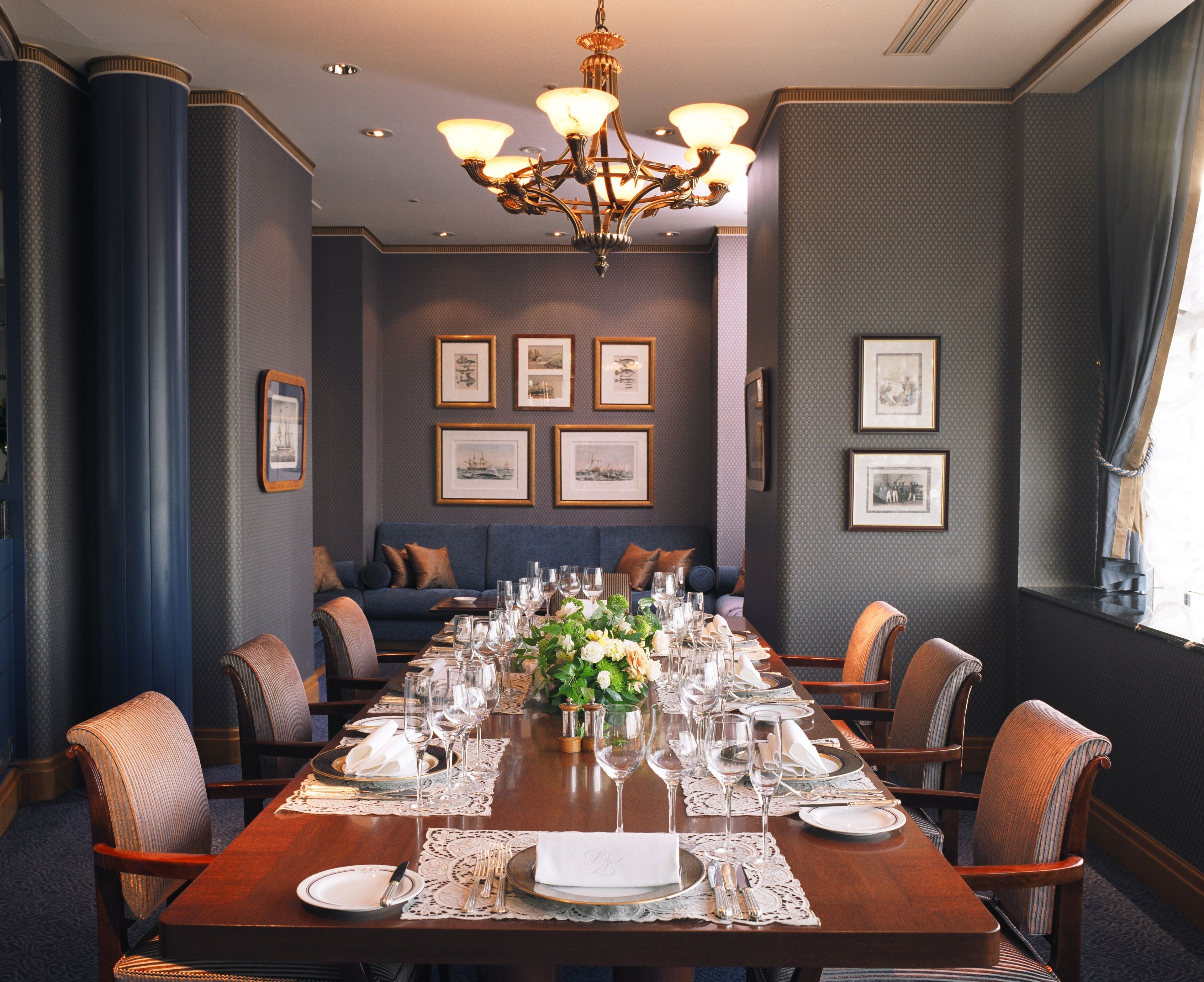 Een formele eetzaal met een lange tafel gedekt voor een maaltijd, ingelijste foto's aan de muur en een kroonluchter.