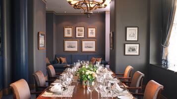 Een formele eetzaal met een lange tafel gedekt voor een maaltijd, ingelijste foto's aan de muur en een kroonluchter.