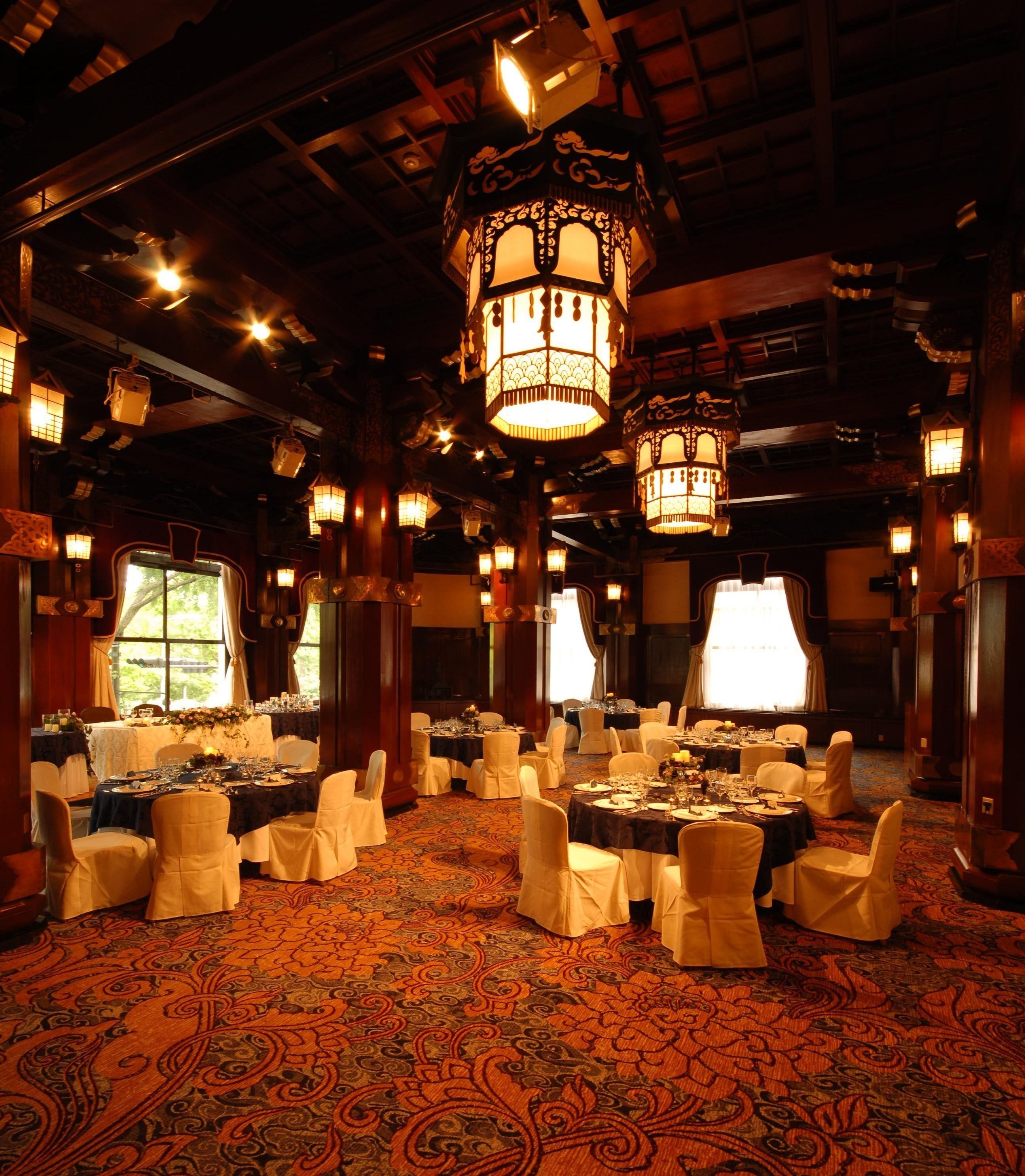 Une salle de banquet avec des tables rondes, des chaises blanches et des lustres décoratifs.