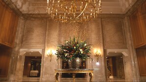 Un vaste hall d’entrée agrémenté d’un grand lustre, d’un arrangement floral au centre d’une table et de murs en marbre.