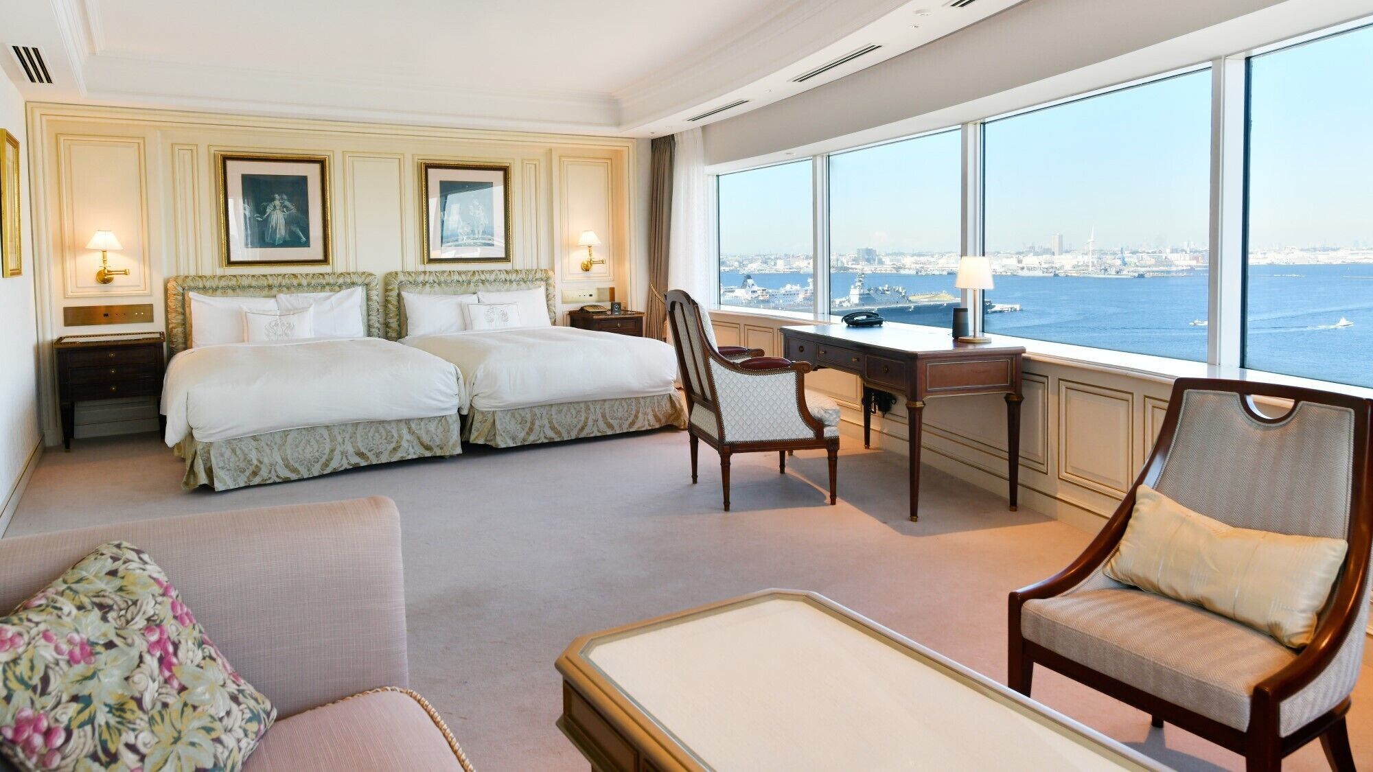 A hotel room with two beds, a desk, a chair, and a view of the city and water.