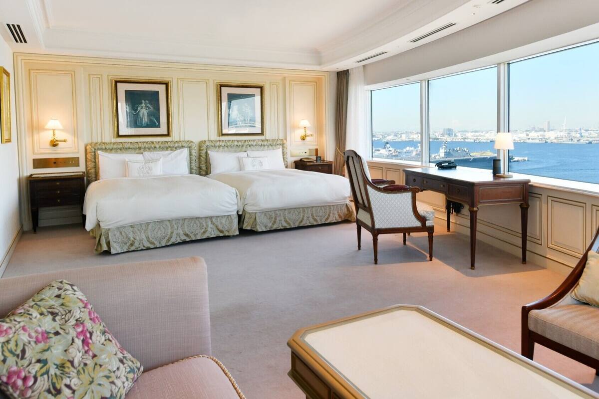 Quarto de hotel com duas camas, uma mesa, uma cadeira e vista para a cidade e para a água.