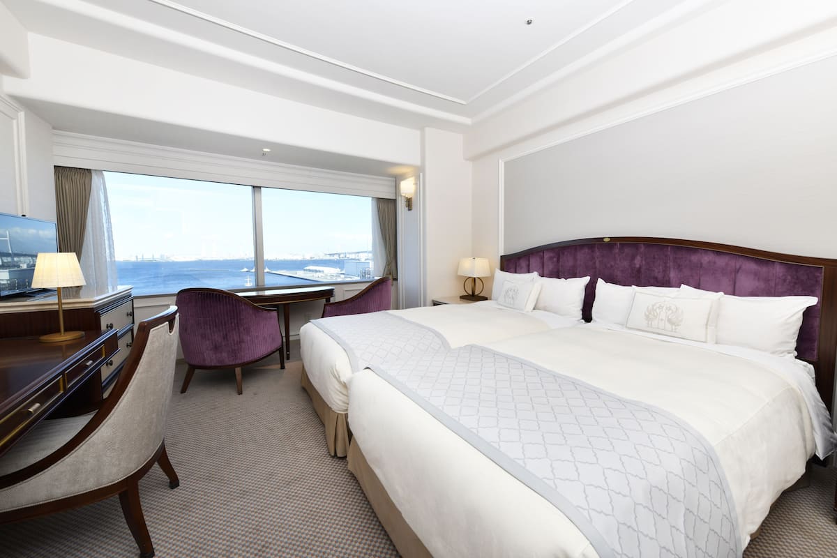 Quarto de hotel com uma cama grande, uma escrivaninha, uma cadeira e vista para a cidade.