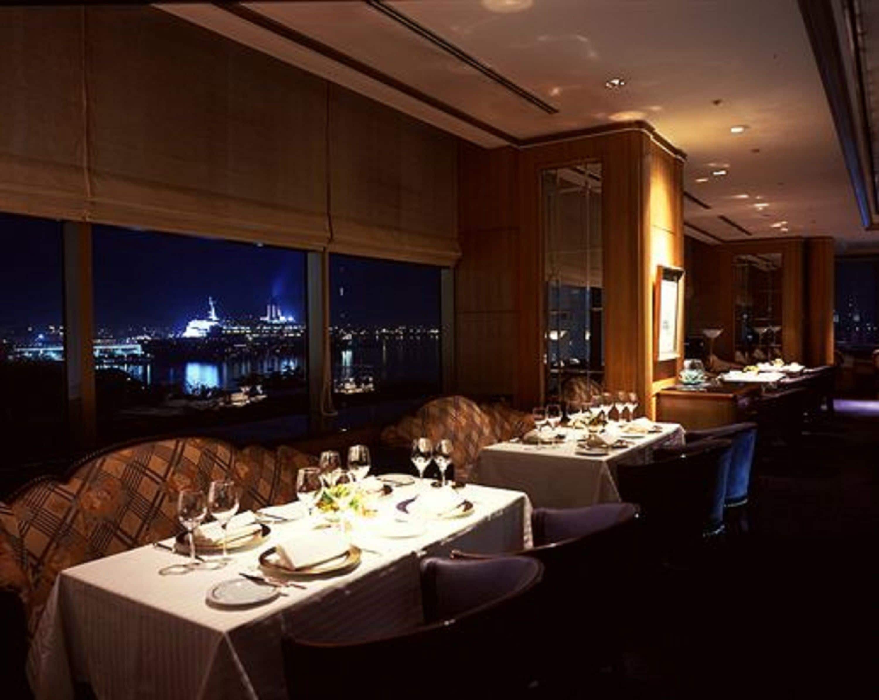 Un restaurante con mesas dispuestas para comer, amplias ventanas que ofrecen vistas a la ciudad y una decoración interior moderna.