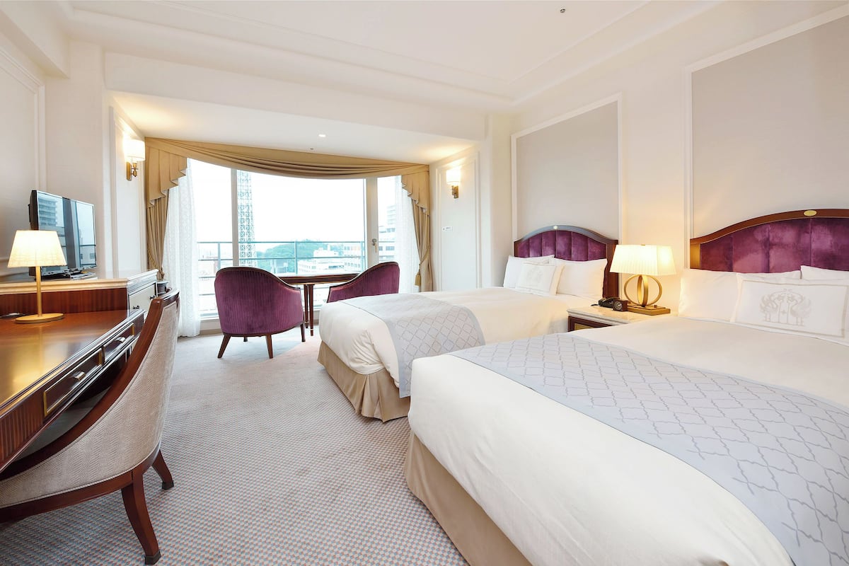 Quarto de hotel com duas camas, uma mesa de trabalho com televisão e uma cadeira.