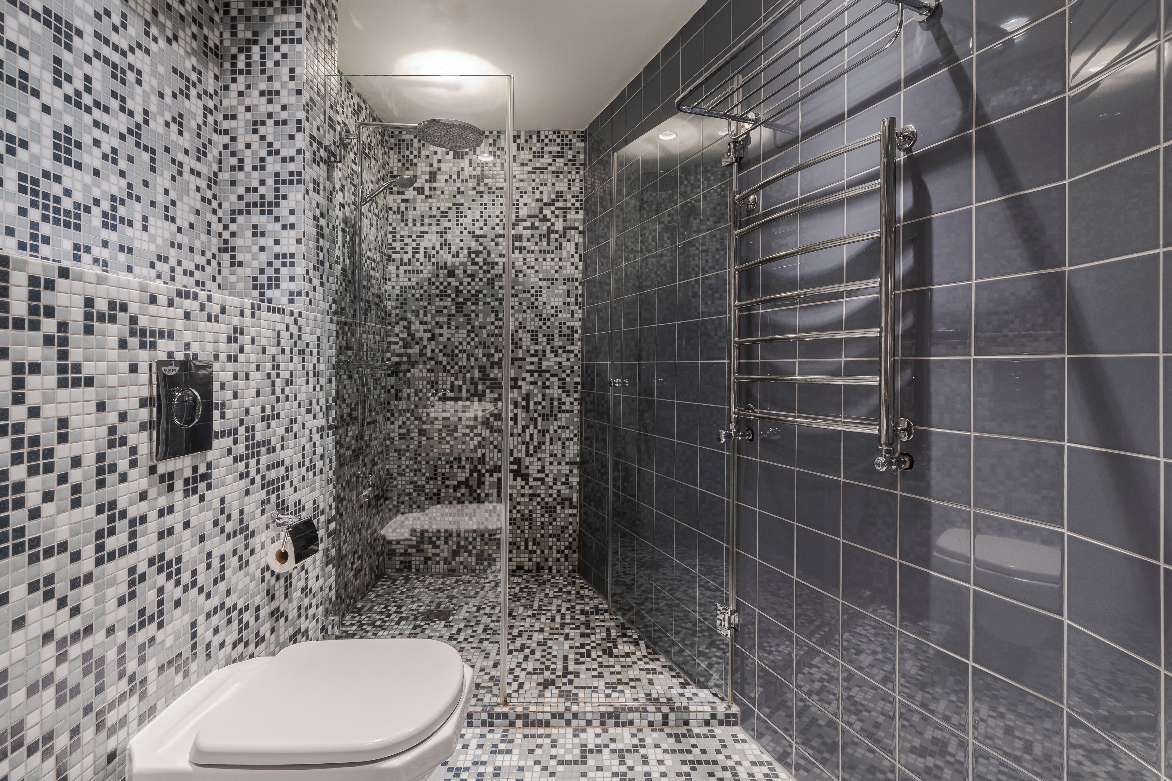 A bathroom with mosaic tile walls, a shower area, and a toilet.