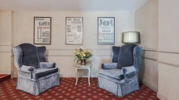 A room with two velvet armchairs, a small table with a vase of flowers, and three framed posters on the wall.
