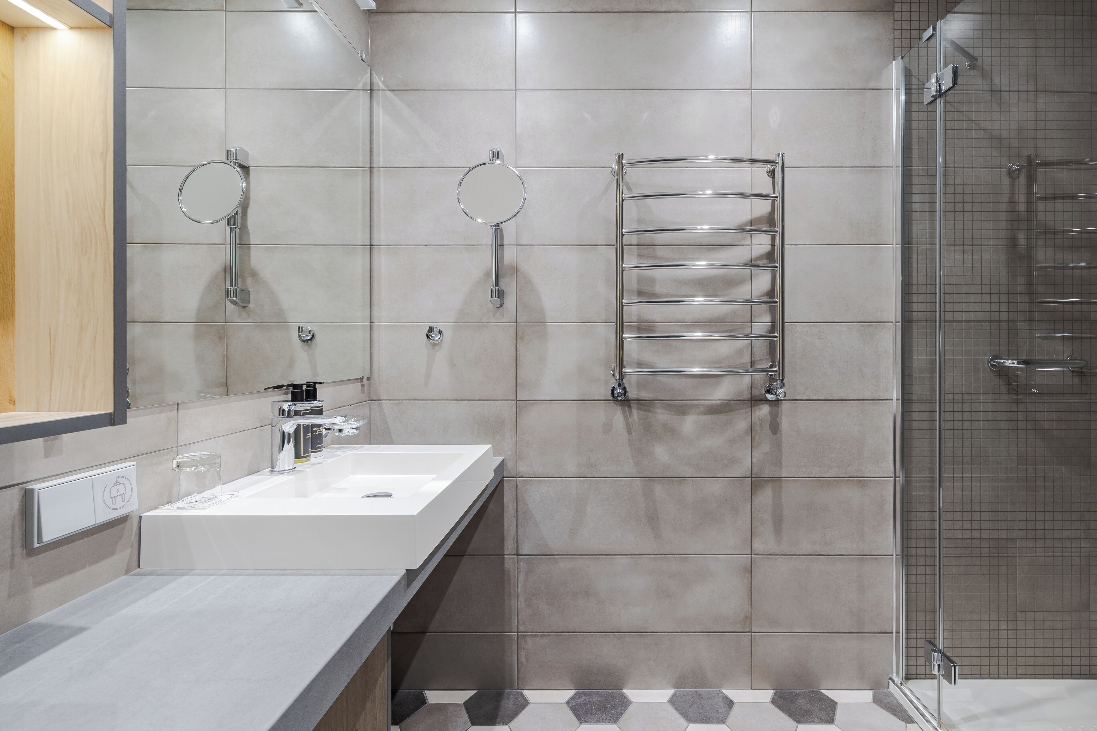 A modern bathroom with a white sink, two round mirrors, a chrome towel rack, and a glass shower enclosure.