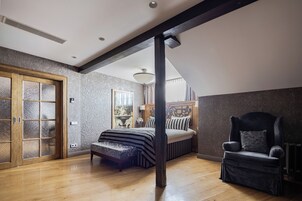 A bedroom with a wooden floor, a bed with a striped bedspread, a dark armchair, and a wooden door with glass panels.