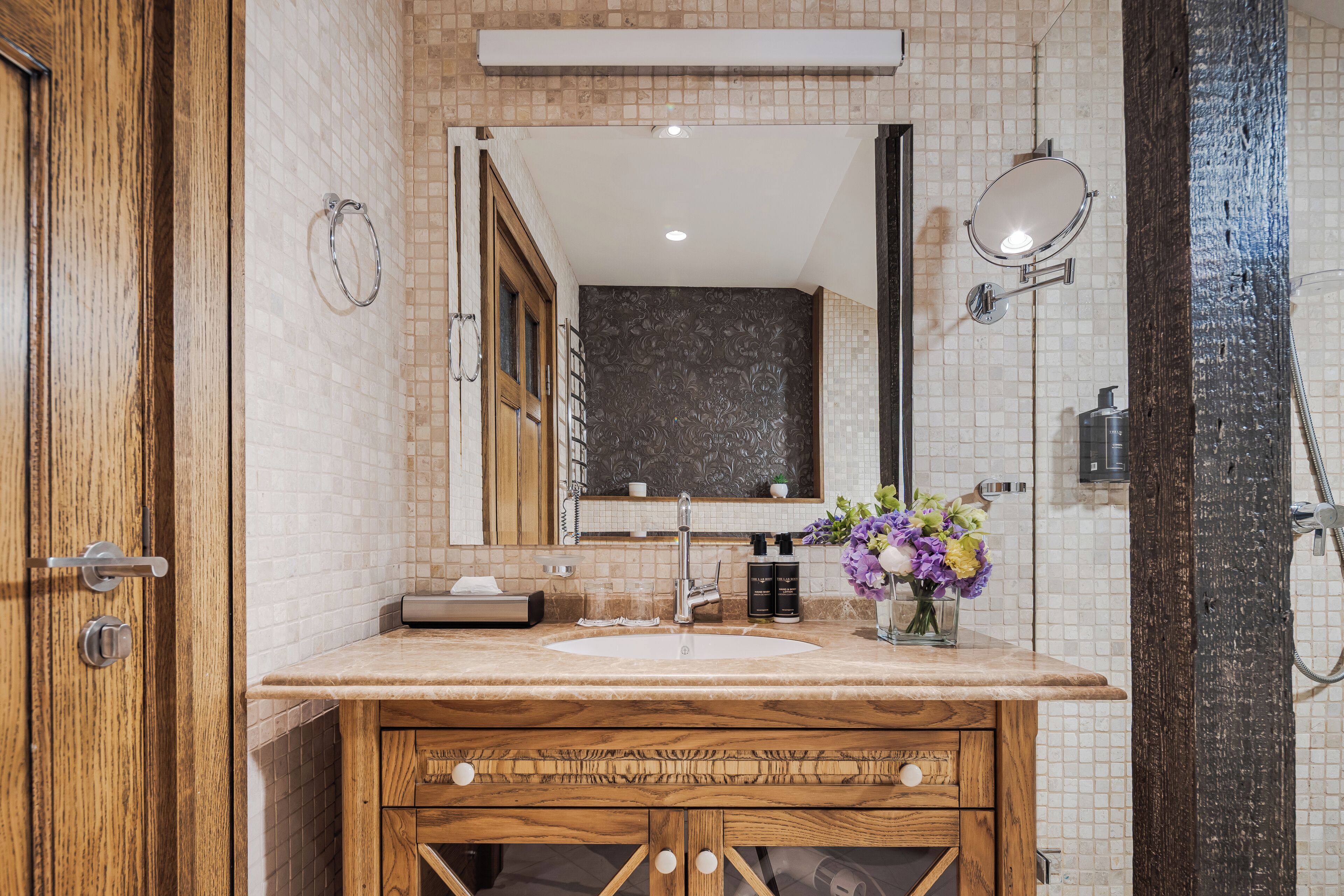 A bathroom with a wooden vanity, a sink, a mirror, and a shower area.